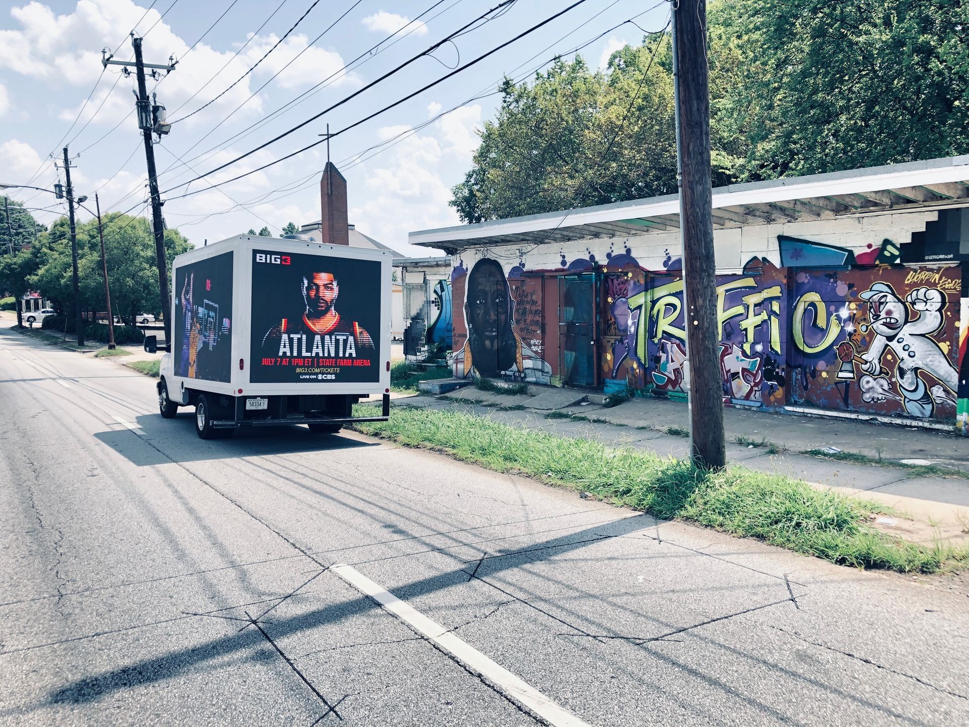 Street scene with a truck displaying an advertisement for Atlanta and colorful graffiti on a building wall.