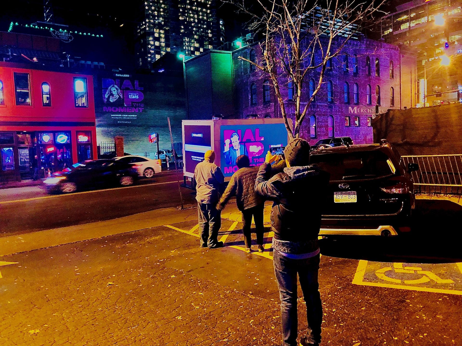 Nighttime street scene with people, illuminated buildings, and neon signs in an urban area.