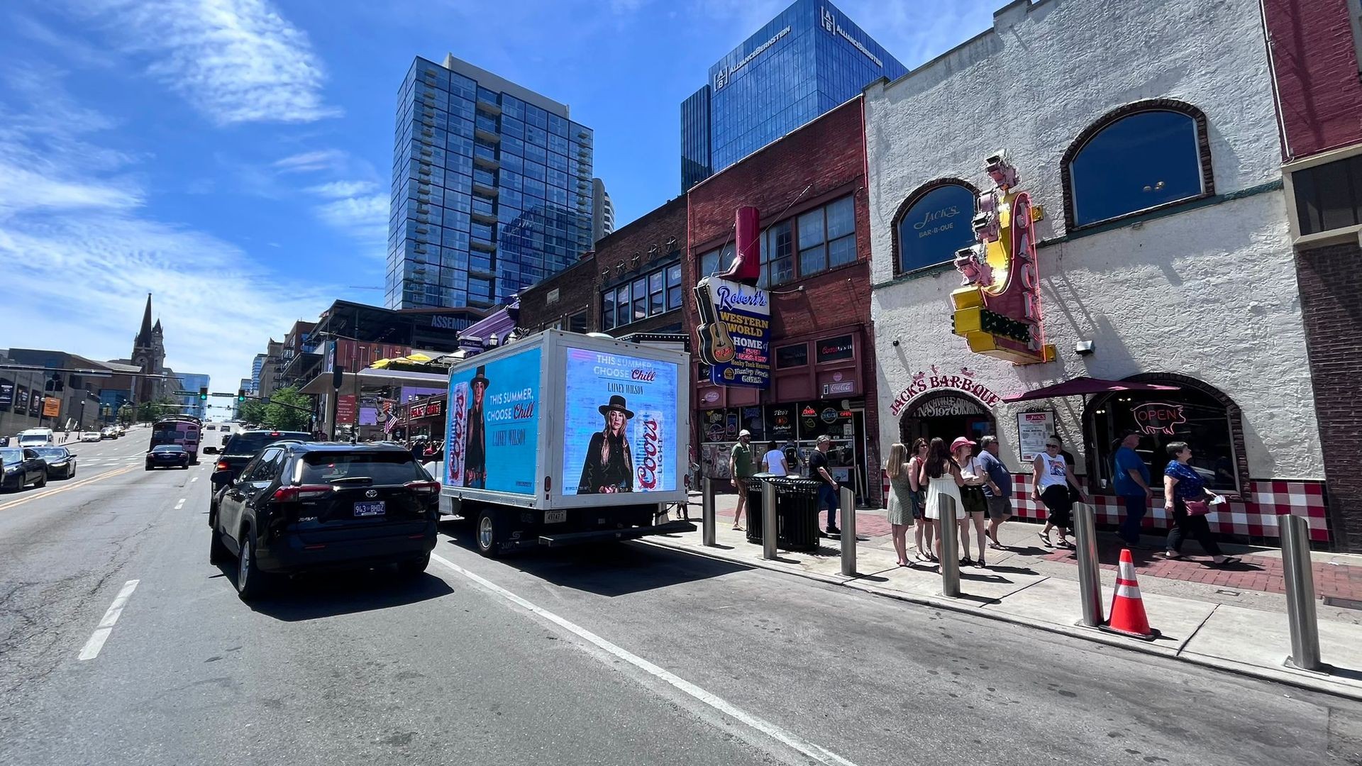 Street view in a city with cars, people, and buildings under a clear blue sky.