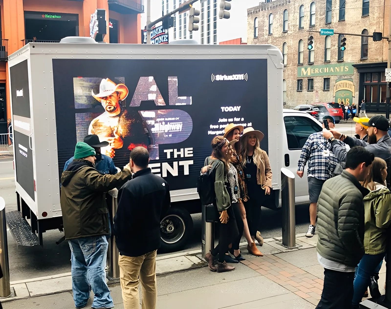 Group of people gathered around a truck with an LED screen advertisement in a city street environment.